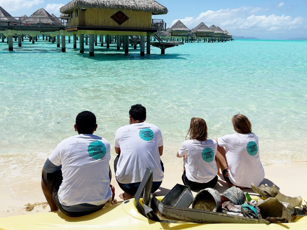 LeMoana_Our-Team_Green-Leaders The Green Leaders team, composed of four people, sitting on a kayak and looking in the direction of the pilings of the InterContinental Le Moana Hotel